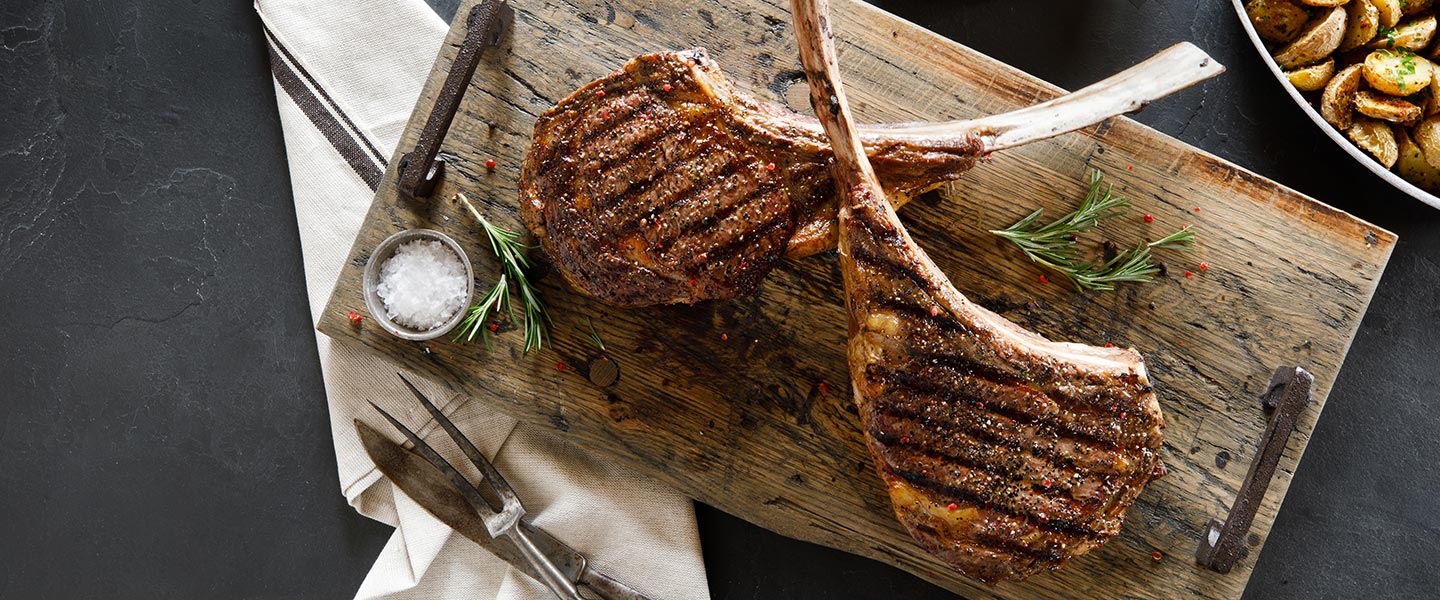 two grilled tomahawk steaks on cutting board
